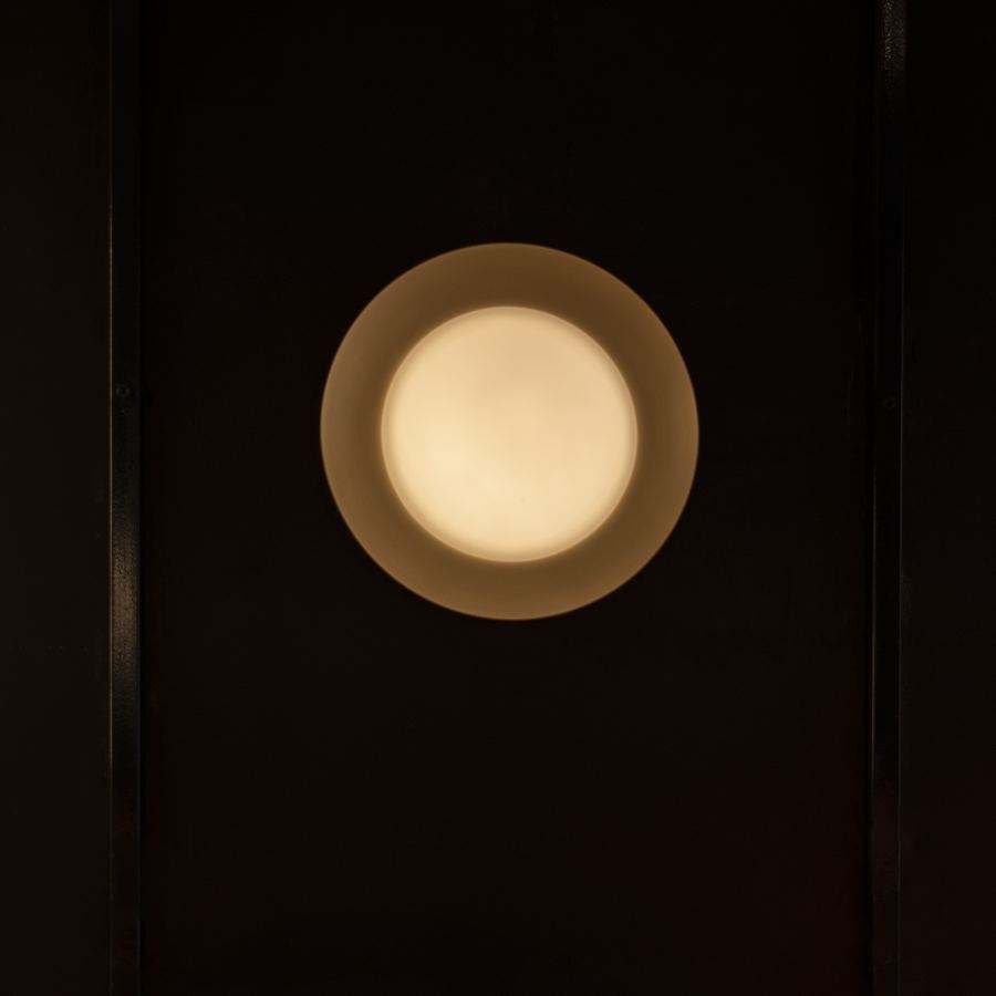 Aplique redondo de plato con el difusor encendido sobre un panel negro.