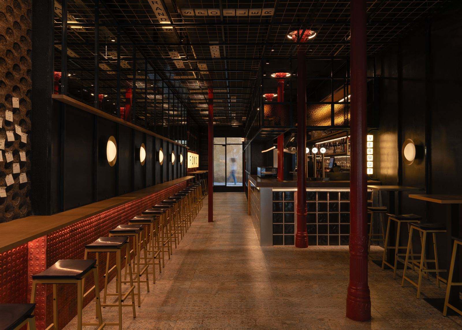 La barra de FOMO Bar: apliques redondos encendidos, frente de azulejo rojo, columnas rojas y la caja de luz VERMUT al fondo.
