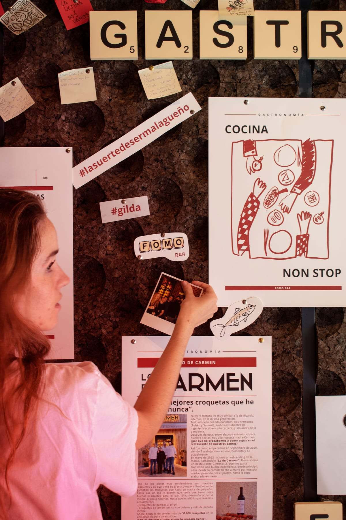 Una clienta clava una nota en el corcho de FOMO Bar, junto al cartel de la carta «COCINA NON STOP».