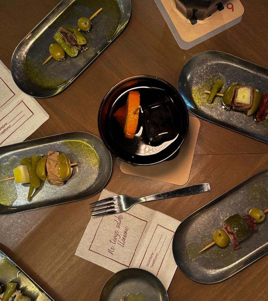 Vista cenital de una mesa de FOMO Bar con varias gildas en bandejitas de metal, un vermut con naranja y servilletas «No tengo saldo. Llámame».