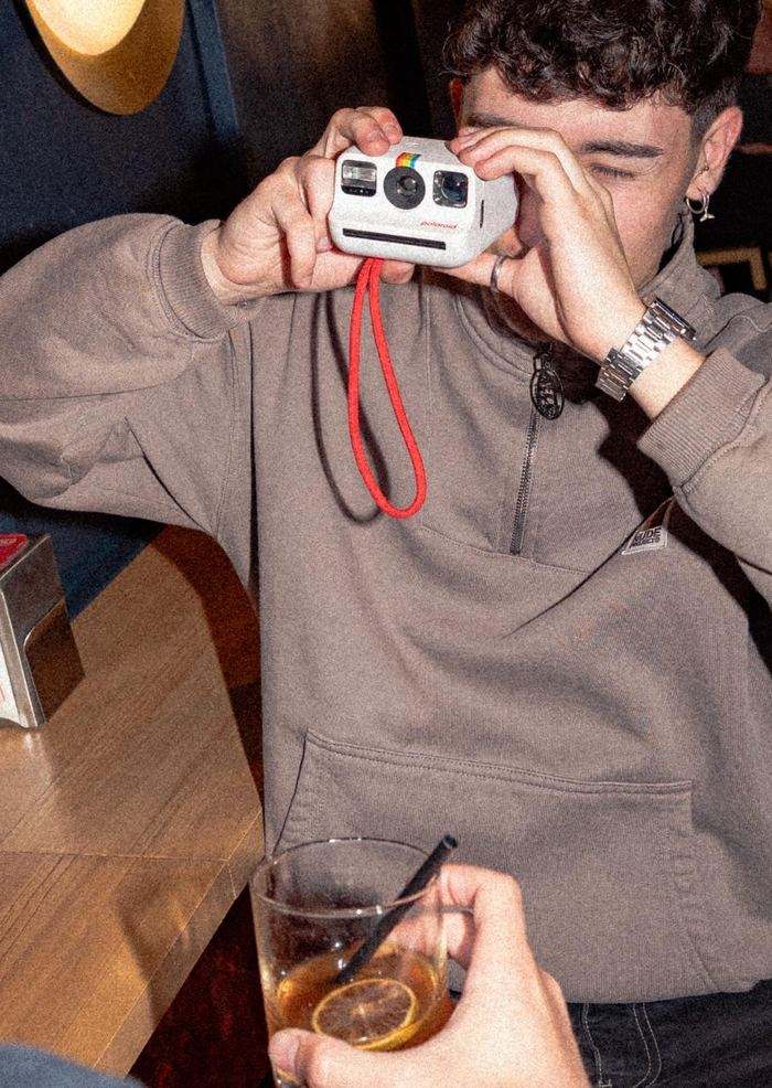 Un cliente hace una foto con una cámara Polaroid en la barra, con flash directo y un vermut en primer plano.
