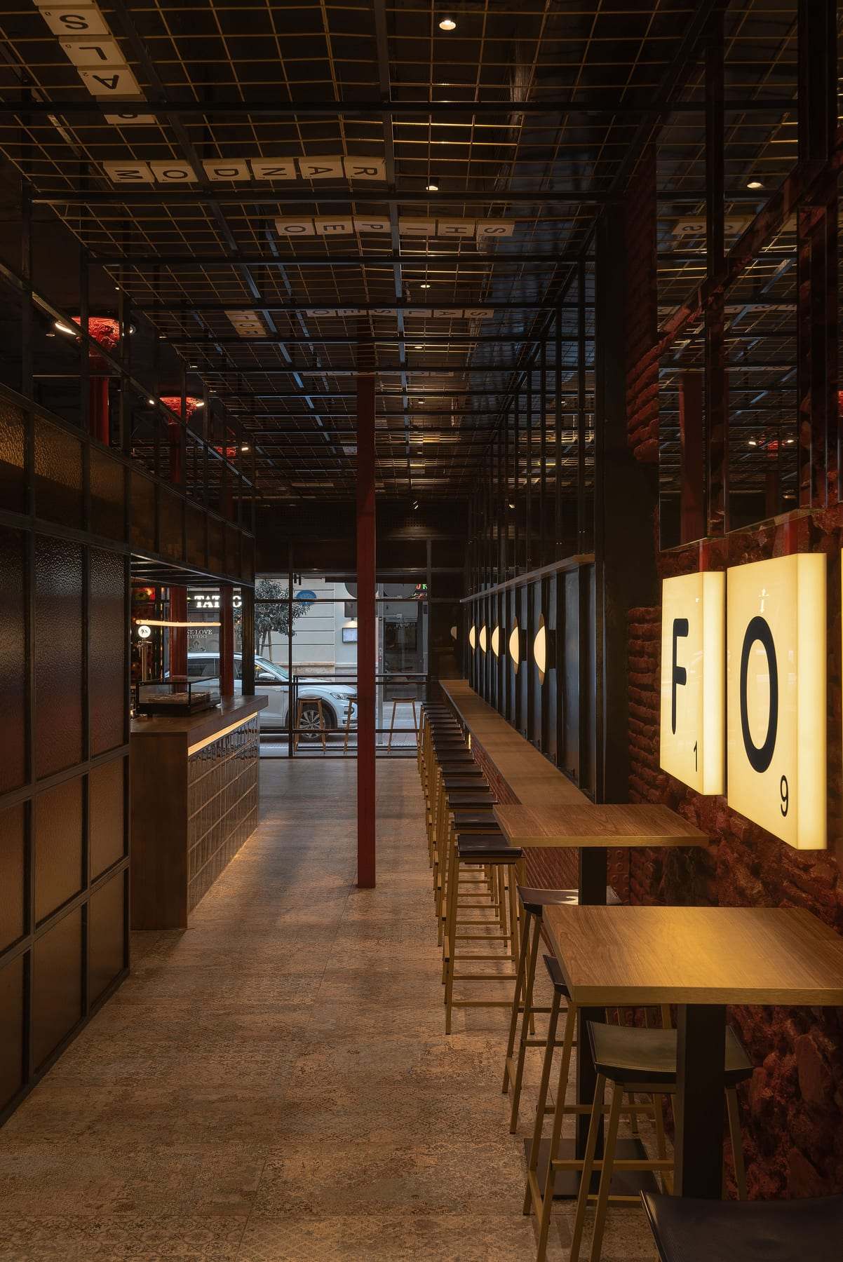 Pasillo de FOMO Bar con mesas altas y taburetes, las cajas de luz F y O en la pared y el techo de rejilla negro.