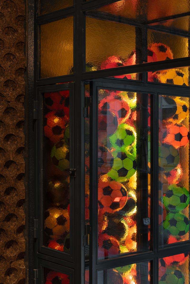 Vidriera retroiluminada llena de balones de fútbol de colores detrás de vidrio martillado y carpintería de acero negro.